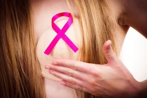 Woman gently touching her chest with a pink ribbon symbol