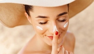 Beautiful Young woman with sun cream on face. Girl holding sunscreen bottle on the beach. Female in hat applying moisturizing lotion on skin.Skin care. Sun protection. Suntan